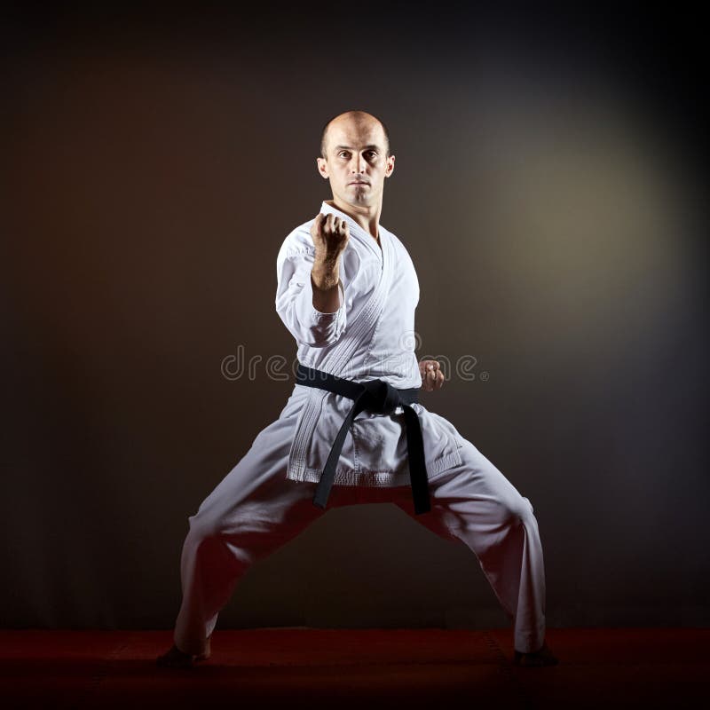 On a dark background athlete trains formally karate exercises royalty free stock photo