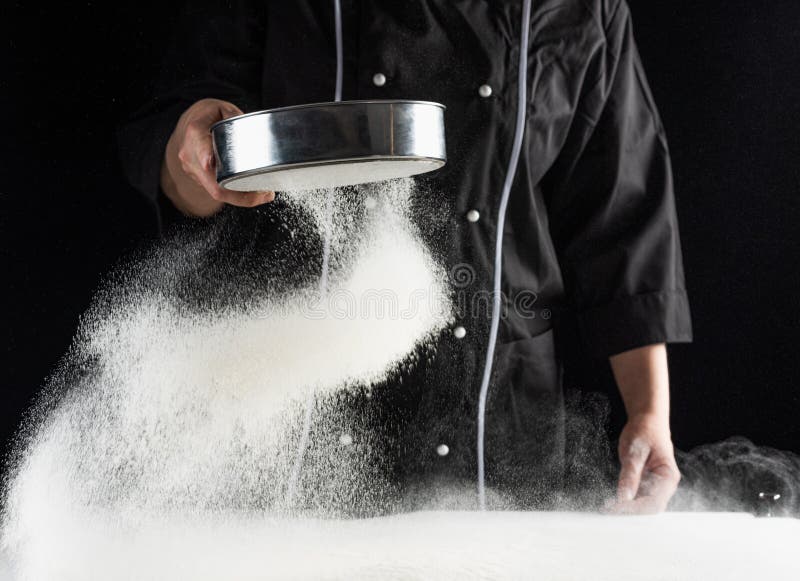 A dark background baker`s hands sift white wheat flour over a sieve over stock photos