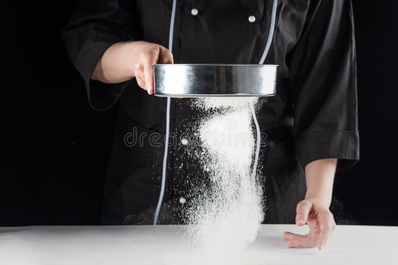 A dark background baker`s hands sift white wheat flour over a sieve over royalty free stock photos