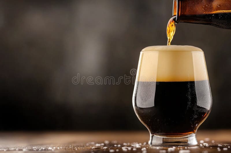 Dark beer pouring into glass on rustic wooden table with foamy head stock photos