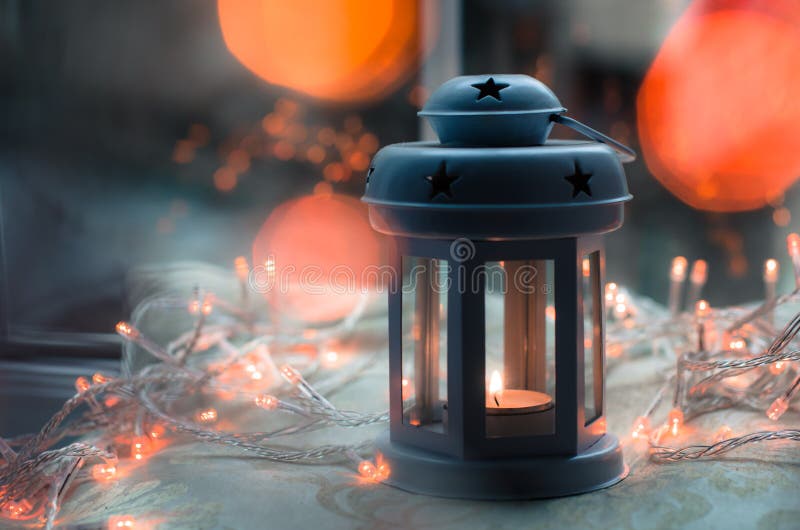 Dark blue and gray candle lantern with blurred orange Christmas lights and bokeh