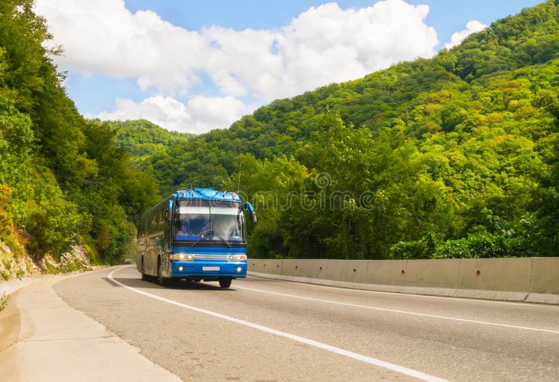 Blu scuro bus turistico va su strada tra le montagne.