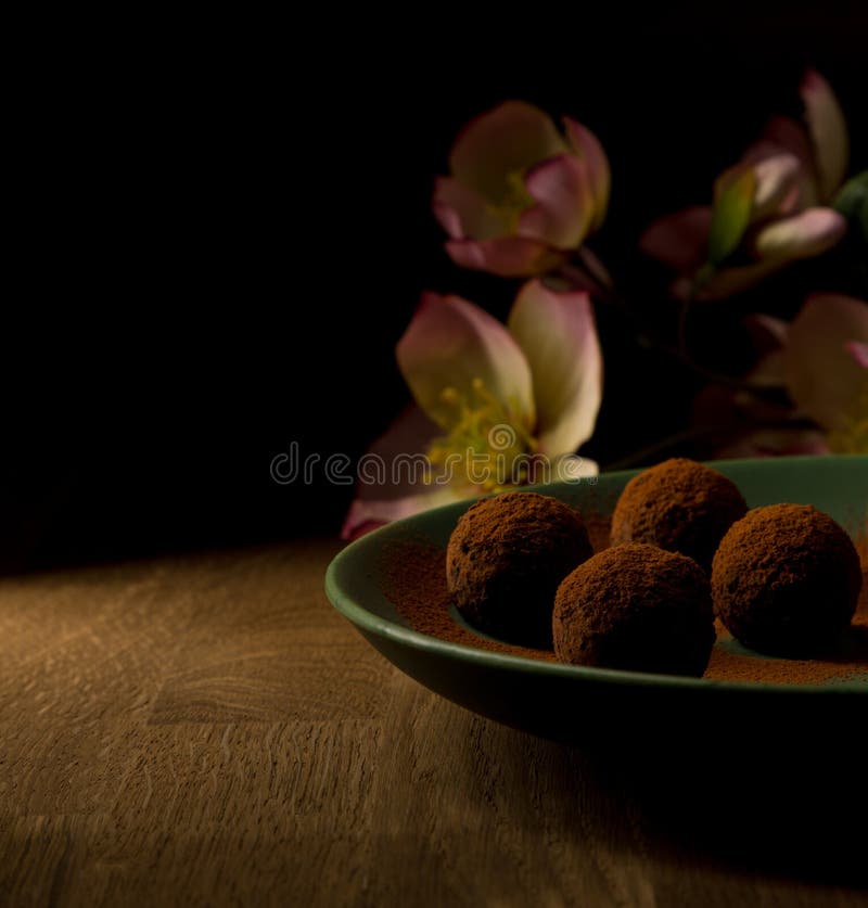 Dark chocolate truffles in green plate on wooden, and pink flowers in background. royalty free stock photo Dark chocolate truffles in green plate on wooden, and pink flowers in background. royalty free stock photo