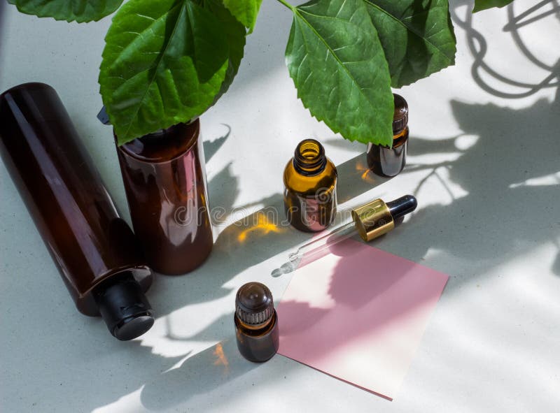 Dark cosmetic bottles and green natural leaves on a light background. Pink blank card, sheet for writing. Layout for adding