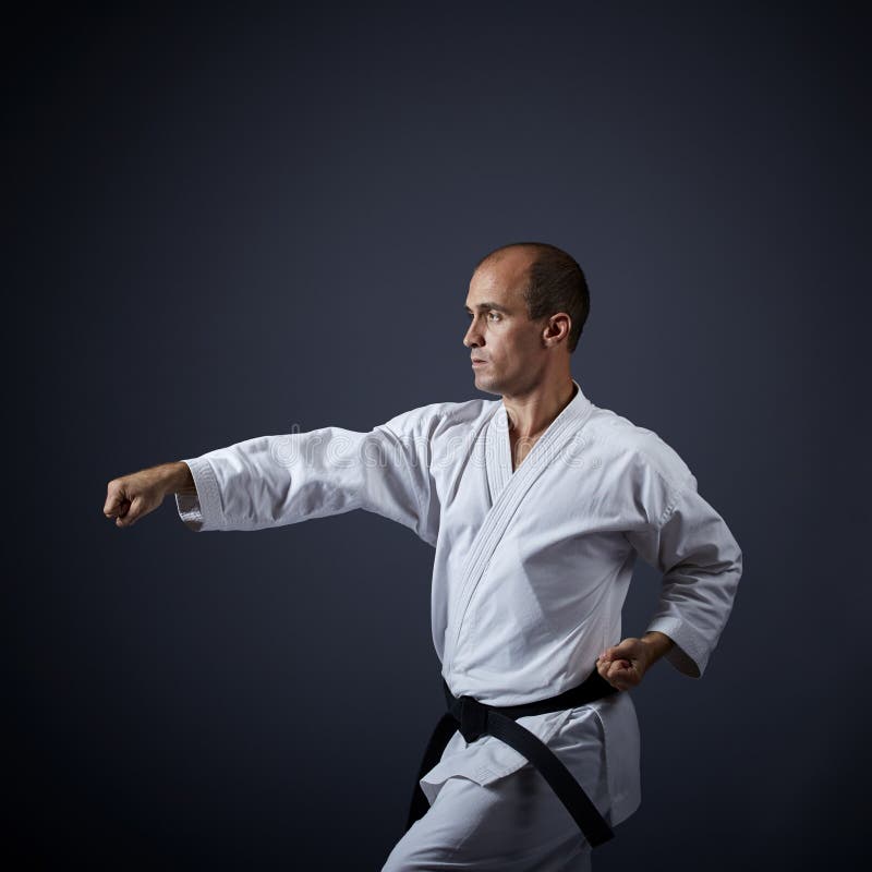 On a dark gray background, a young athlete performs formal karate exercises. royalty free stock photography
