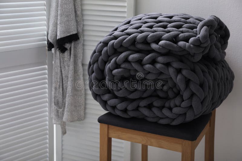 Dark Grey Chunky Knit Blanket Rolled on Wooden Stool in Room Stock