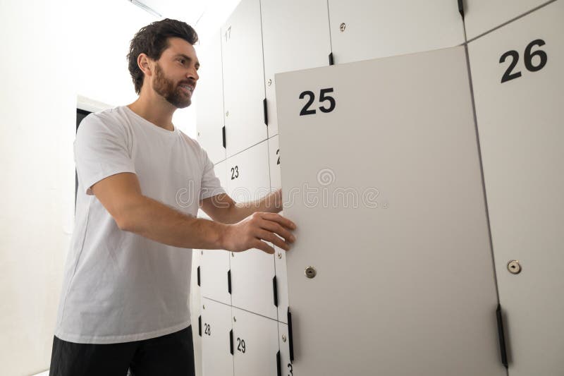 Dark-haired bearded man in changing room in gym stock photo