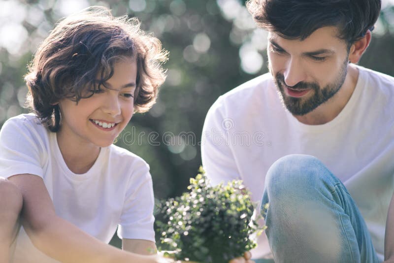 Dark-haired boy and his dad looking at the plant and smiling royalty free stock photo