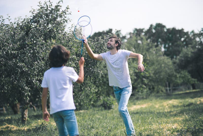 Dark-haired boy and his father playing badminton and looking excited stock photo