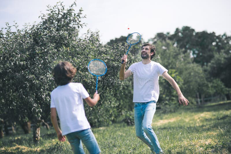 Dark-haired boy and his father playing badminton and looking involved royalty free stock photography