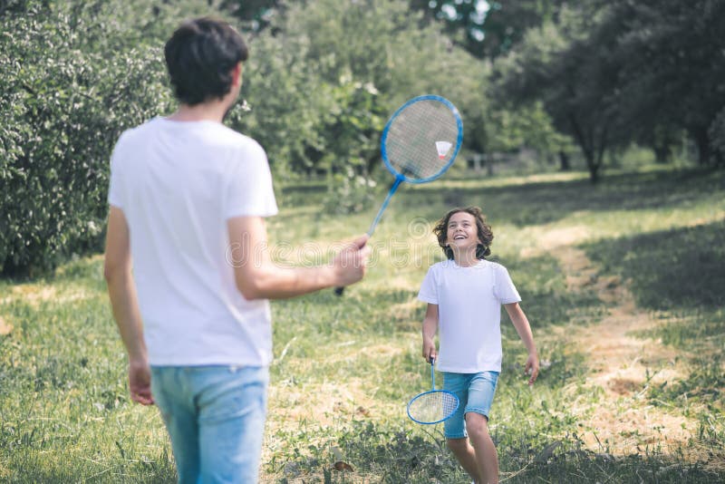 Dark-haired boy and his father playing badminton in the park stock image