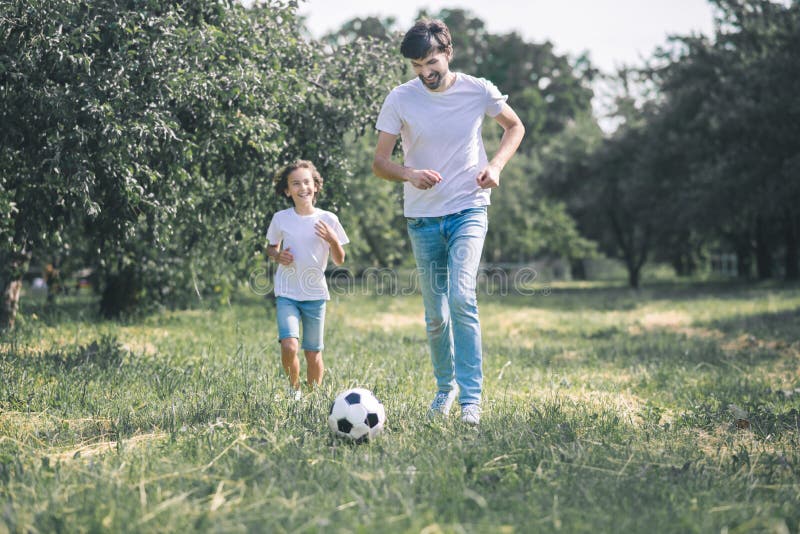Dark-haired boy and his father playing with the ball stock photography