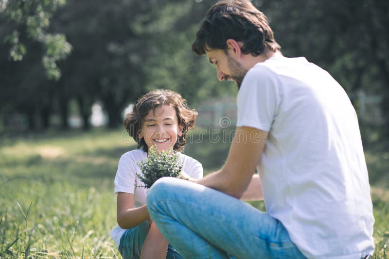 Dark-haired boy smiling and holding the plant, his father sitting near him stock image