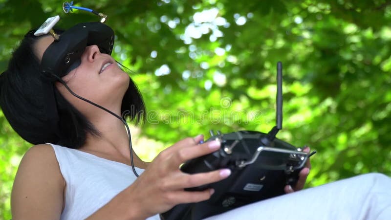 The dark-haired girl sits at the nature and emotionally controls the racing drone through virtual reality glasses