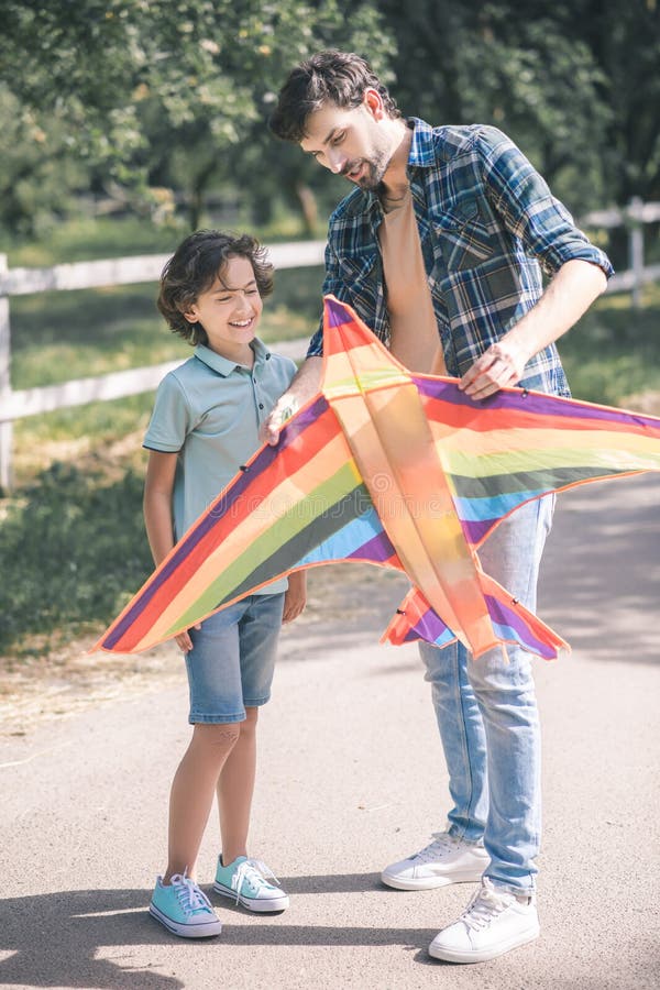 Dark-haired man holding a colorful kite and explaining to his son how to use it stock image