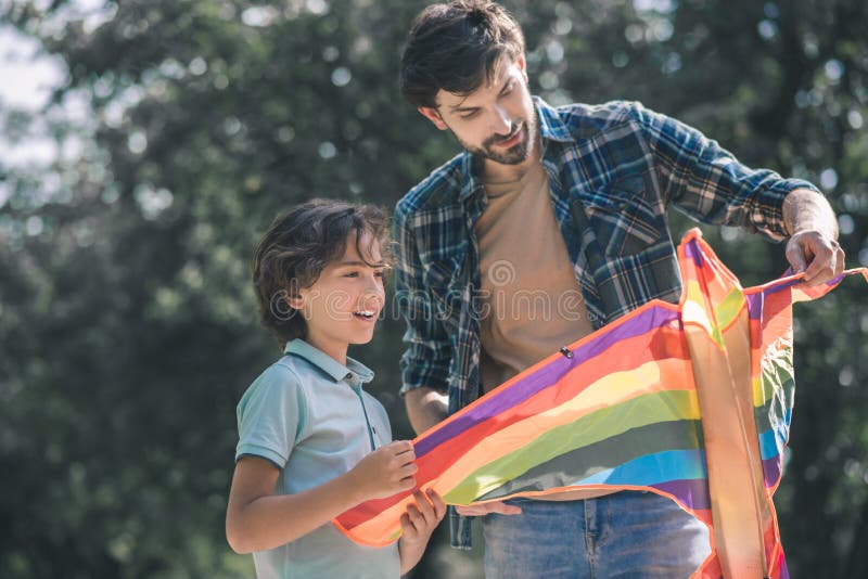 Dark-haired man holding a colorful kite and showing it to his son royalty free stock photos
