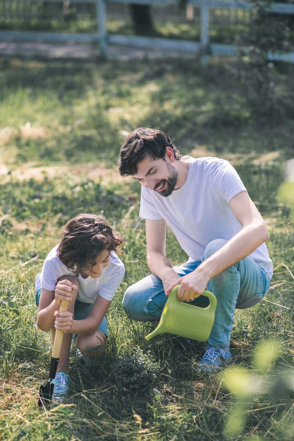 Dark-haired man watering the plant, his son watching him stock image