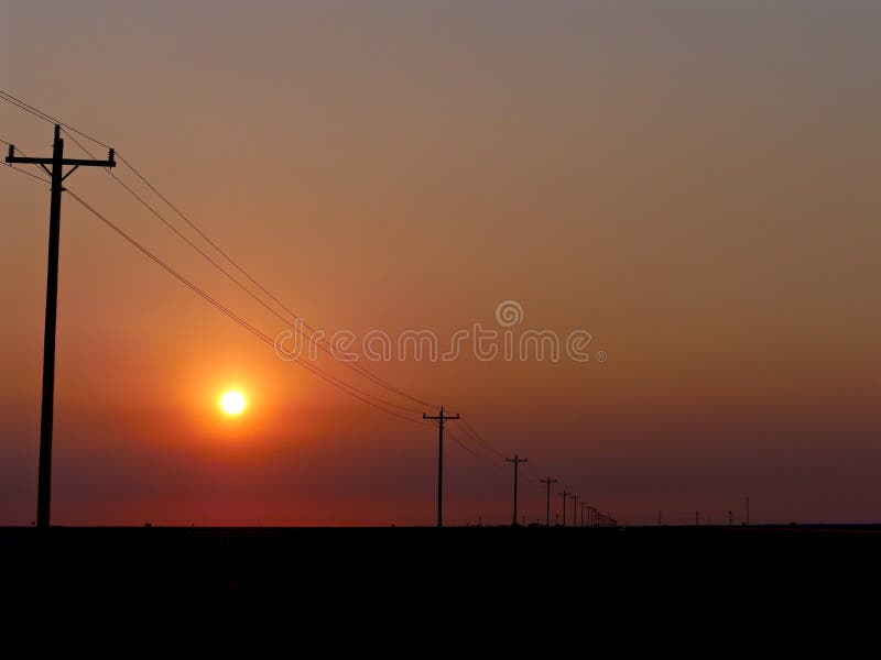 Dark orange setting sun over flat land, receding utility poles to infinity