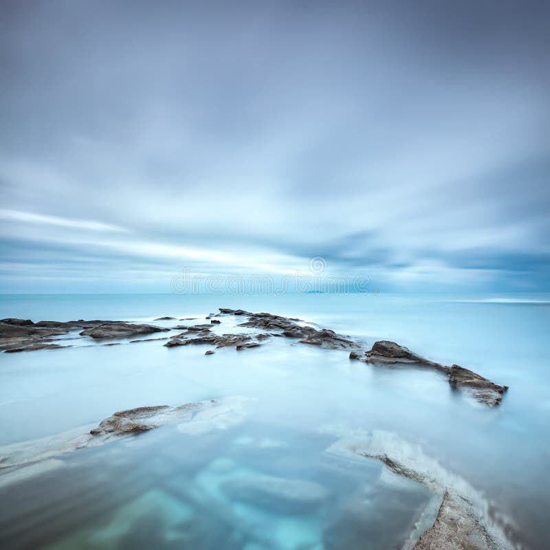 Dark rocks in a blue ocean under cloudy sky in a bad weather. Long exposure photography