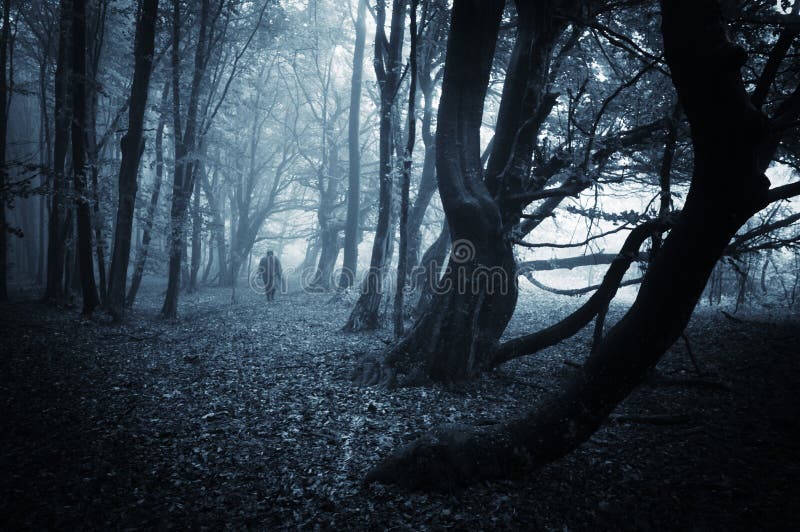 Dark scene of a spooky man walking in a dark forest with blue fog on halloween