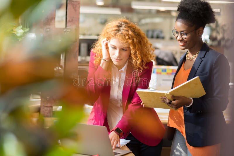 Dark-skinned assistant standing near boss using laptop royalty free stock photo