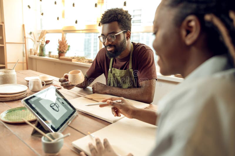 Bărbat cu pielea închisă care are un atelier pe ceramică și care ascultă cu atenție femeile profesioniste stock photo