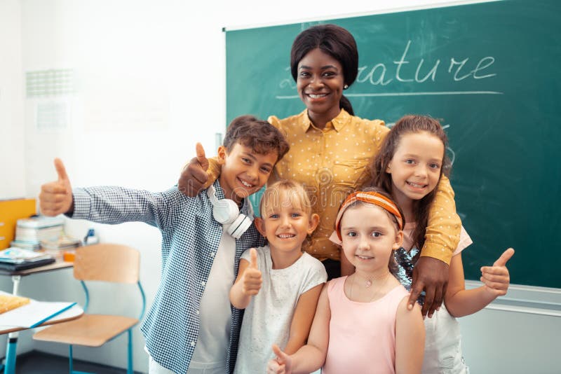 Dark-skinned teacher feeling cheerful with her funny smart pupils royalty free stock images