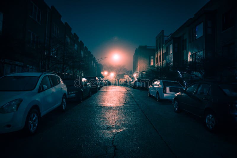 Dark wet and foggy city street with cars at night.