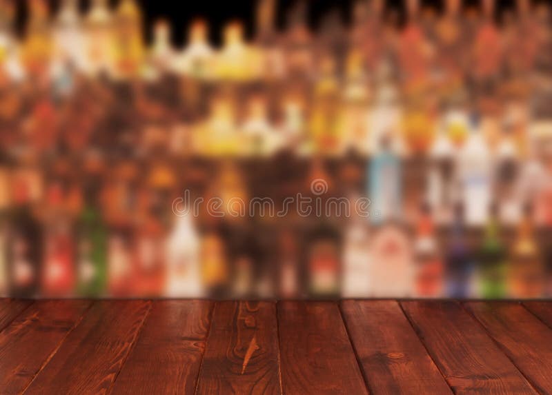 Dark wooden table against interior of bar with alcohol bottles