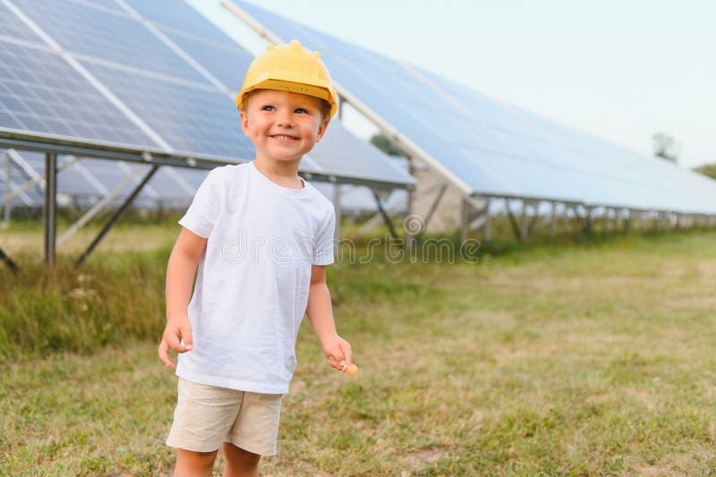 Darstellung eines Kindes in der Nähe der Solarzellen. ein kleiner Junge in einem Schutzhelm in der Nähe von Sonnenkollektoren mit lizenzfreies stockbild