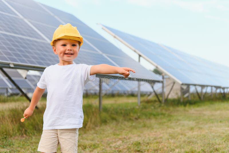 Darstellung eines Kindes in der Nähe der Solarzellen. ein kleiner Junge in einem Schutzhelm in der Nähe von Sonnenkollektoren mit stockfotografie