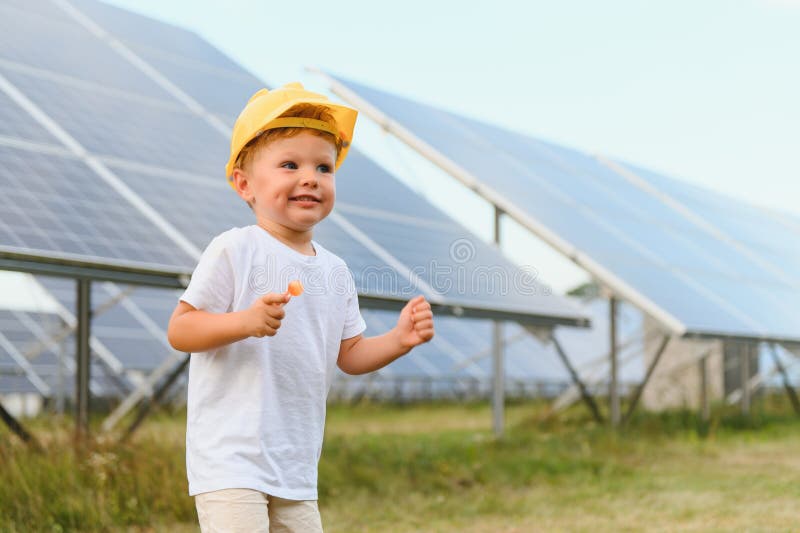 Darstellung eines Kindes in der Nähe der Solarzellen. ein kleiner Junge in einem Schutzhelm in der Nähe von Sonnenkollektoren mit stockfotografie