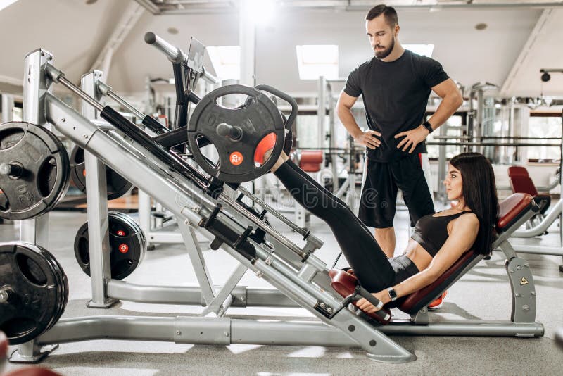 Das athletische Mädchen, das in der schwarzen Sportkleidung gekleidet wird, hebt Gewichte mit ihren Beinen in der Turnhalle unter stockfotografie