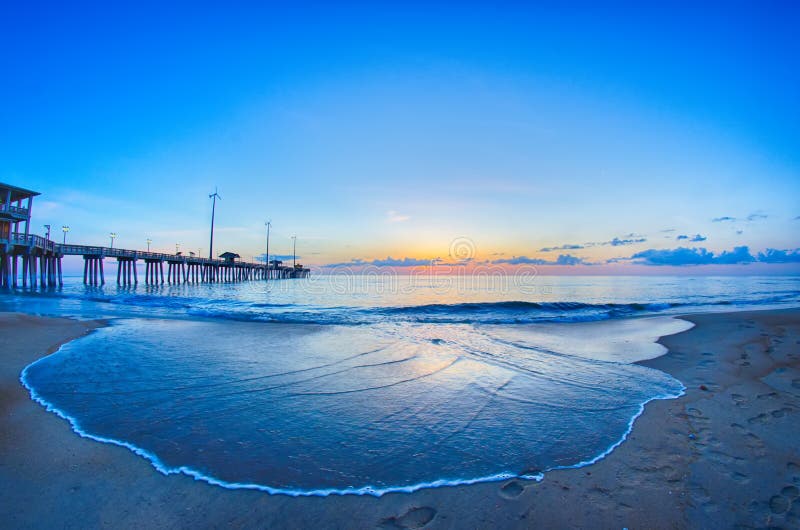 The rising sun peeks through clouds and is reflected in waves by the Nags Head fishing pier on the outer banks of North Carolina. The rising sun peeks through clouds and is reflected in waves by the Nags Head fishing pier on the outer banks of North Carolina