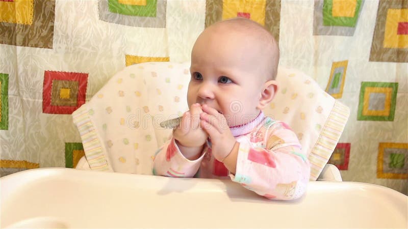 Das Baby sitzt in einem Stuhl für das Essen und hält einen Löffel in seiner Hand