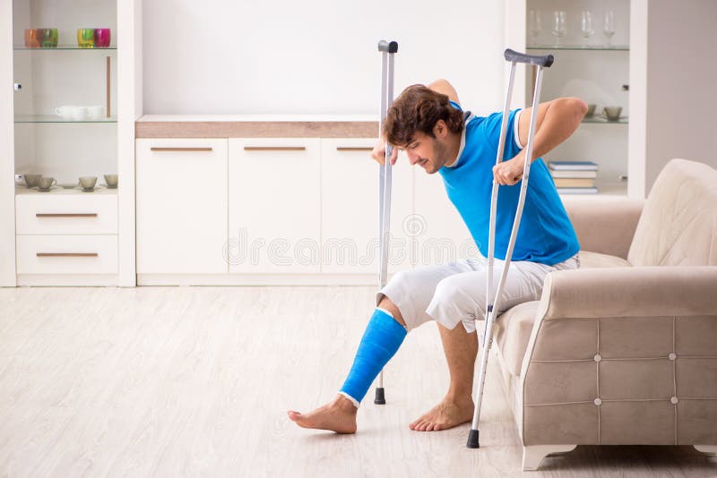 Das Bein verletzte jungen Mann mit Krücken zu Hause lizenzfreies stockbild