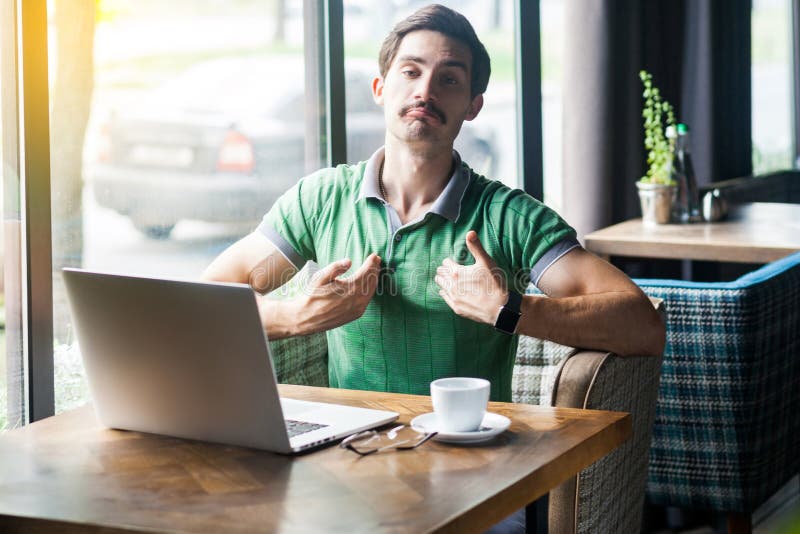 Das bin ich! Junge stolze, hochmütige Geschäftsleute in grünem T-Shirt sitzen mit Laptop und schauen Kamera mit stolzem, selbstbe lizenzfreies stockfoto