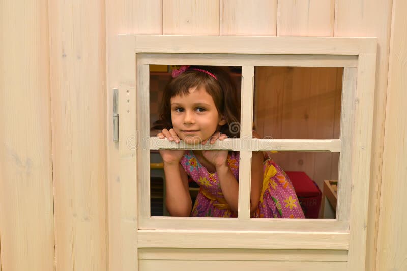 Das fünfjährige Mädchen schaut heraus in einem Häuschenfenster kindergarten lizenzfreies stockbild Das fünfjährige Mädchen schaut heraus in einem Häuschenfenster kindergarten lizenzfreies stockbild