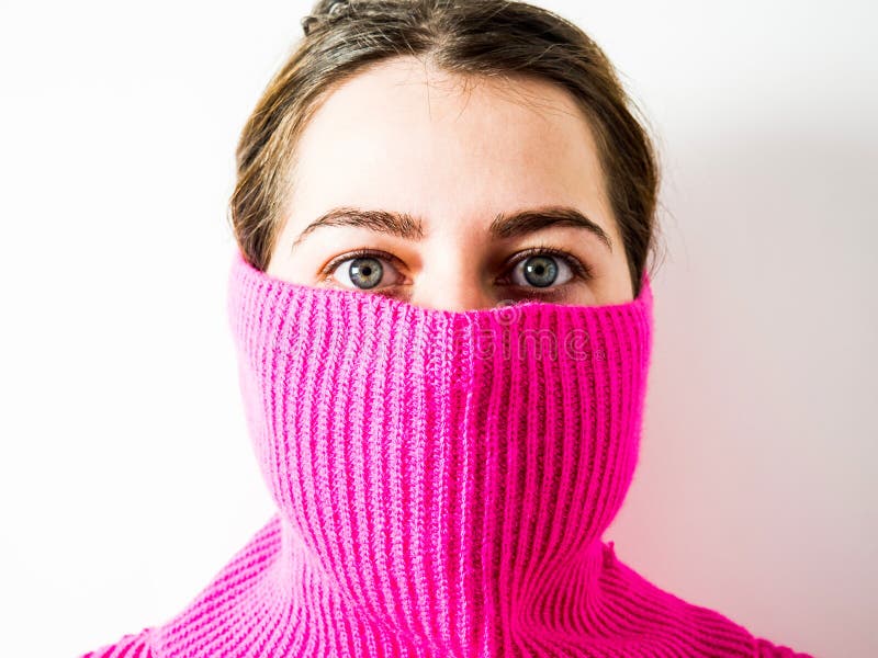 Das Gesicht eines schönen Mädchens, das von einem rosa Pullover bedeckt ist
