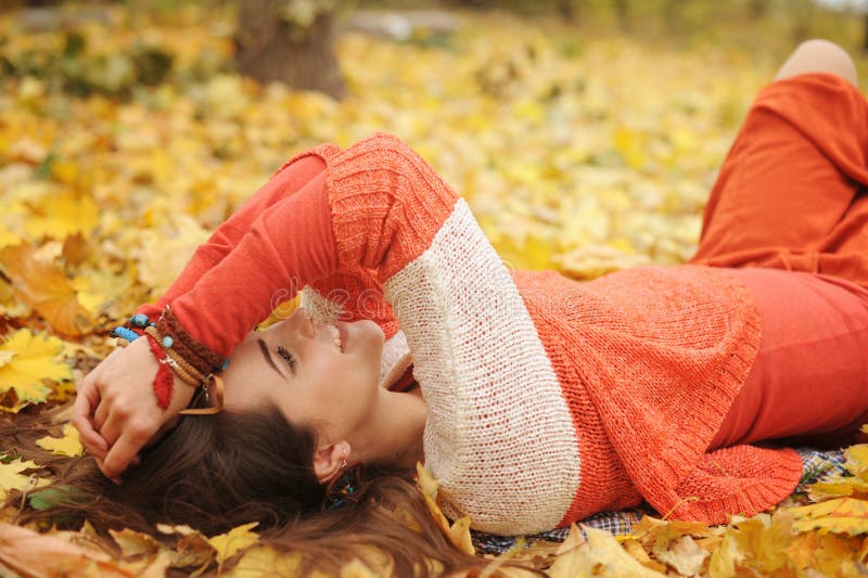 Happy resting girl portrait, lying in autumn maple leaves in park, closed eyes, dressed in fashion sweater and many friendship bracelets, outdoor. Happy resting girl portrait, lying in autumn maple leaves in park, closed eyes, dressed in fashion sweater and many friendship bracelets, outdoor