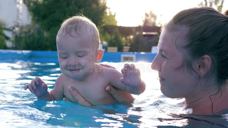 Das glückliche lächelnde Kleinkindhandeln spritzt im Pool, Mutter und Kind haben zusammen Spaß im Sommer