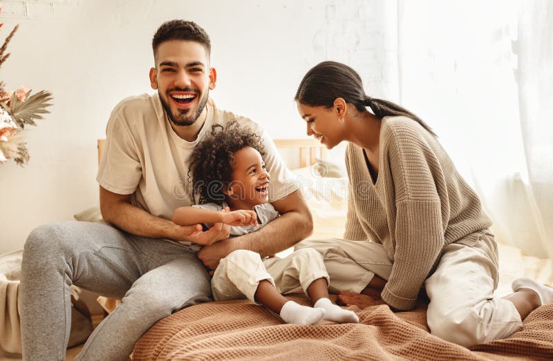 Das glückliche Multi ethnische lachende Spielen des Familienmuttervatis und -kindes und kitzelt im Bett zu Hause. Der Muttervaters und -sohns der glücklichen Familie kitzelt die Multi ethnische lachende Spielen und im Bett im Schlafzimmer zu Hause