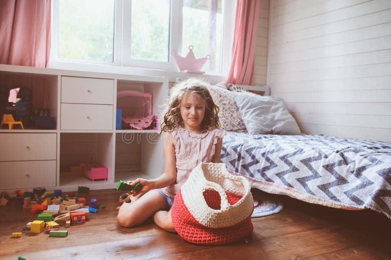 Das Kindermädchen, das ihren Raum säubert und organisieren hölzerne Spielwaren in gestrickte Speichertasche stockfoto Das Kindermädchen, das ihren Raum säubert und organisieren hölzerne Spielwaren in gestrickte Speichertasche stockfoto