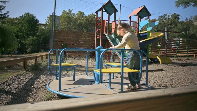 Das kleine hübsche blonde Mädchen, das auf ein fröhliches dreht, gehen Runde am Spielplatz