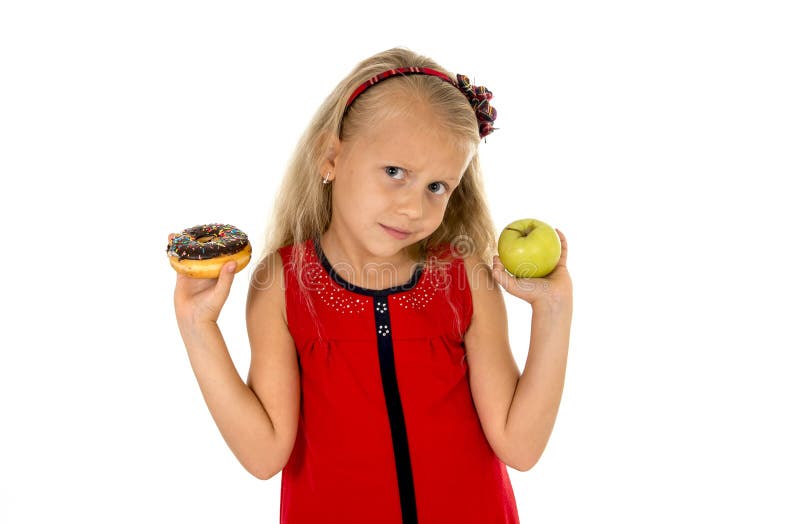 Little beautiful female child with blond hair choosing dessert holding unhealthy but tasty chocolate donut and apple fruit in healthy versus unhealthy die nutrition on white background. Little beautiful female child with blond hair choosing dessert holding unhealthy but tasty chocolate donut and apple fruit in healthy versus unhealthy die nutrition on white background