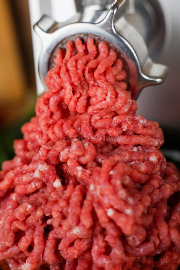 Das Konzept einer gesunden und gesunden Ernährung. Eine Aussicht von oben auf rotes Rindfleisch mit Streifen aus Fett. Eine Nahansicht von oben aus rotem gemahlenem Rindfleisch mit Streifen Fett, die aus dem Metallschleifer in Wellen kommen und den größten Teil des Fotos aufnehmen. Hochwertiges Foto.