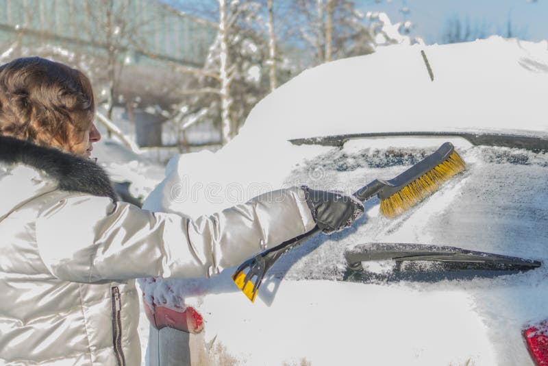 Das Mädchen bürstet die Windschutzscheibe des Autos vom Schnee Wi stockbilder