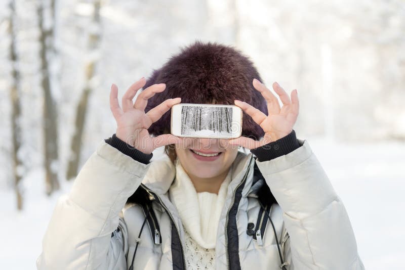 Das Mädchen im Pelzhut hält das Telefon auf Augenhöhe Auf Th stockfoto