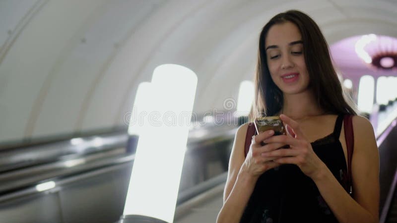 Das Mädchen, das oben auf Rolltreppe in der Metro mit Licht schön ist, las Mitteilung im Telefonlächeln