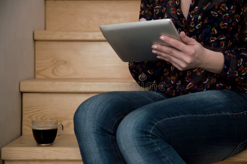 Das Mädchen sitzt und betrachtet den Schirm der Tablette, liest die Nachrichten, trinkt Kaffee Arbeit zu Hause Geschäftsfrau zu H lizenzfreies stockbild Das Mädchen sitzt und betrachtet den Schirm der Tablette, liest die Nachrichten, trinkt Kaffee Arbeit zu Hause Geschäftsfrau zu H lizenzfreies stockbild
